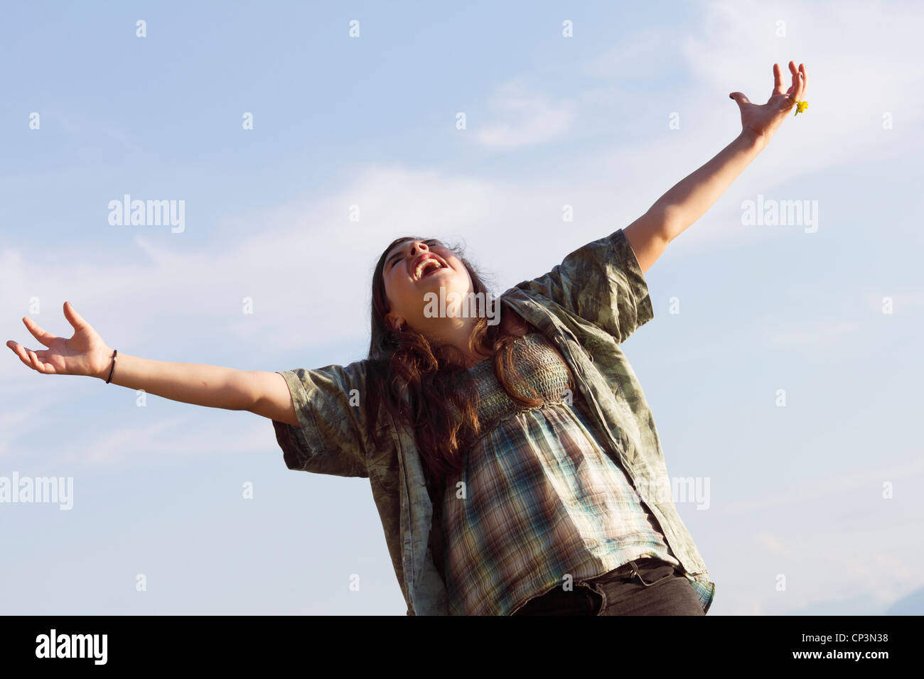 Cry out for joy - young teenage girl with raised arms feeling free. Sunny summer outdoor shot against a blue sky. Stock Photo