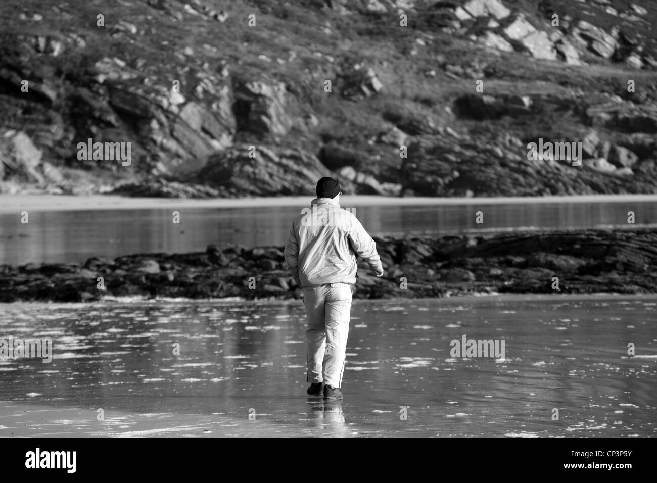 Black & white shot of man with outdoor clothing on crossing a beach just after the tide has gone out Stock Photo