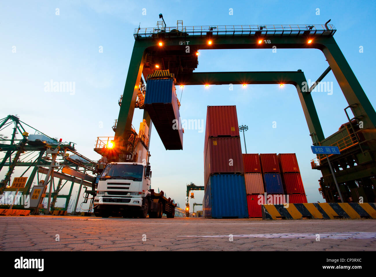 Cranes, cargo containers and trucks at a shipping port during dusk ...