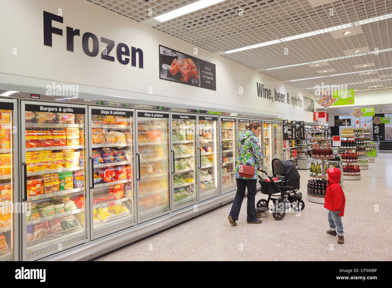 Woman pushing a pram with son shopping in a supermarket frozen food aisle. Stock Photo