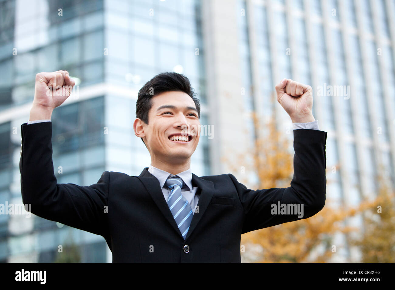 A businessman outside office buildings with his arms raised in ...