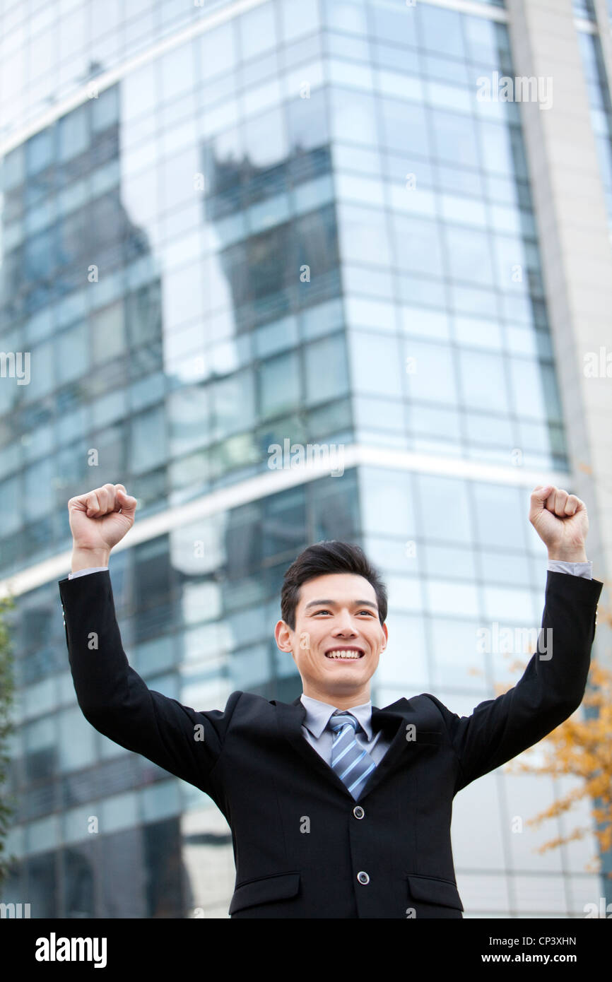 A businessman outside office buildings with his arms raised in ...