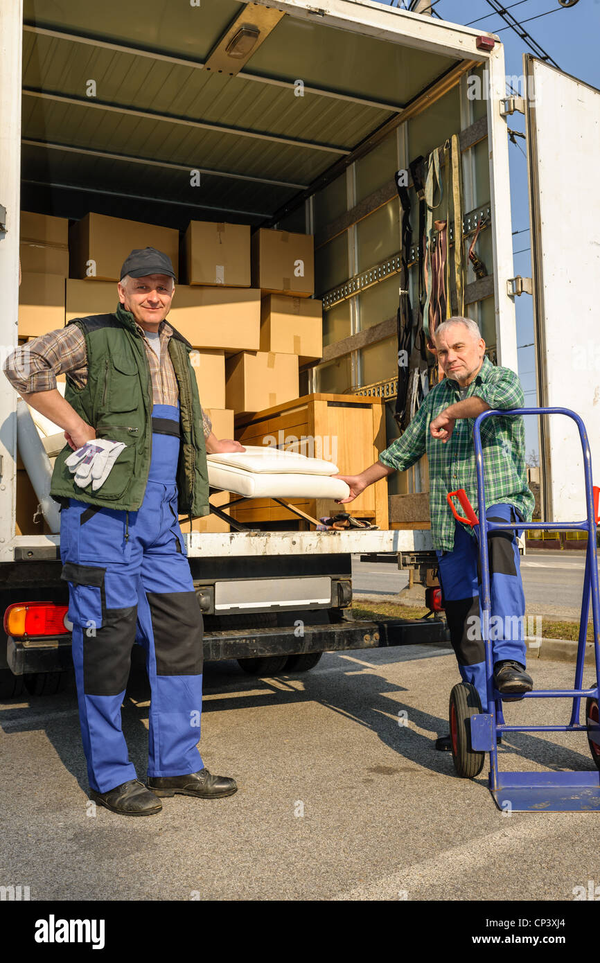 Two male movers unload furniture and boxes from moving truck Stock Photo