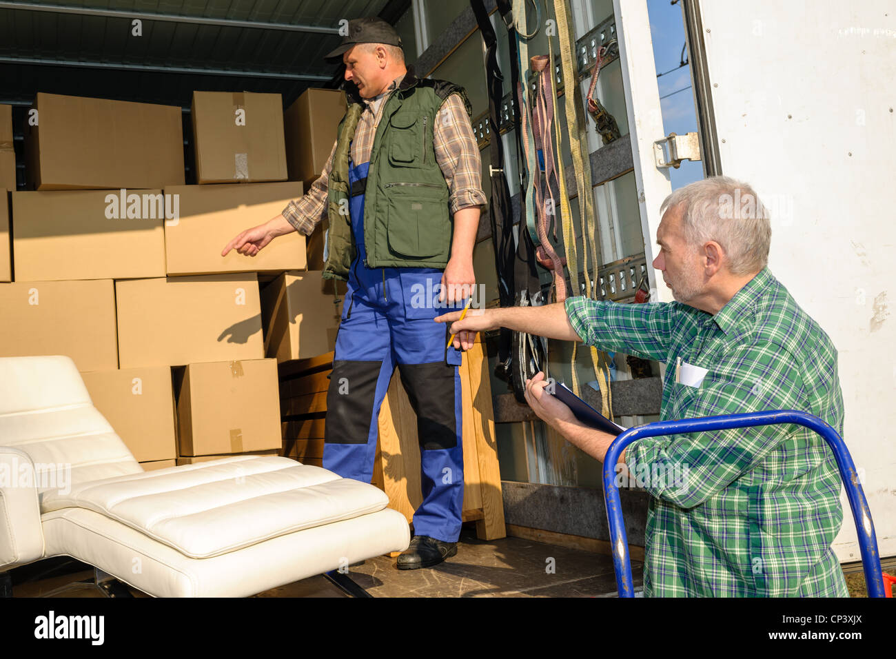 Two male movers unload furniture and boxes from moving truck Stock