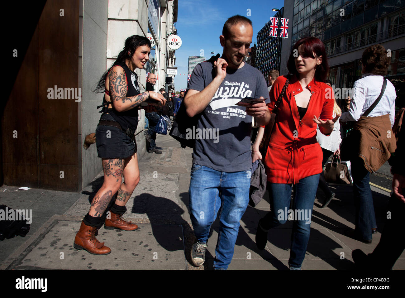 Woman giving out flyers for a tattoo shop to shoppers in central London on Oxford Street. UK. Listening to music she was dancing whilst happily giving out information and chatting to potential Woman giving out flyers for a tattoo shop to shoppers in central London on Oxford Street. UK. Listening to music she was dancing whilst happily giving out information and chatting to potential