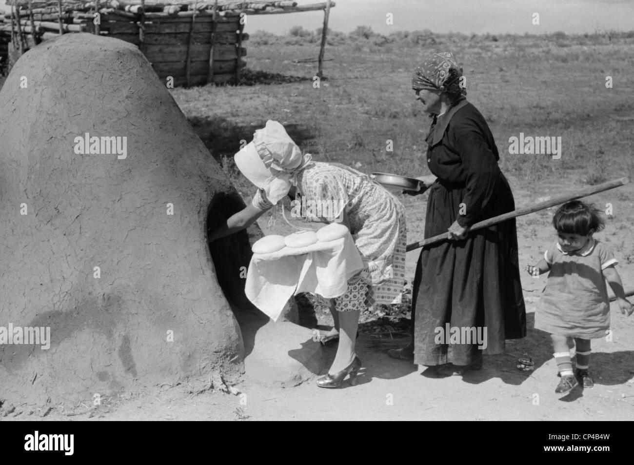 Two Spanish-American women placing loaves of bread in outdoor earthen oven for baking, Taos County, New Mexico Stock Photo
