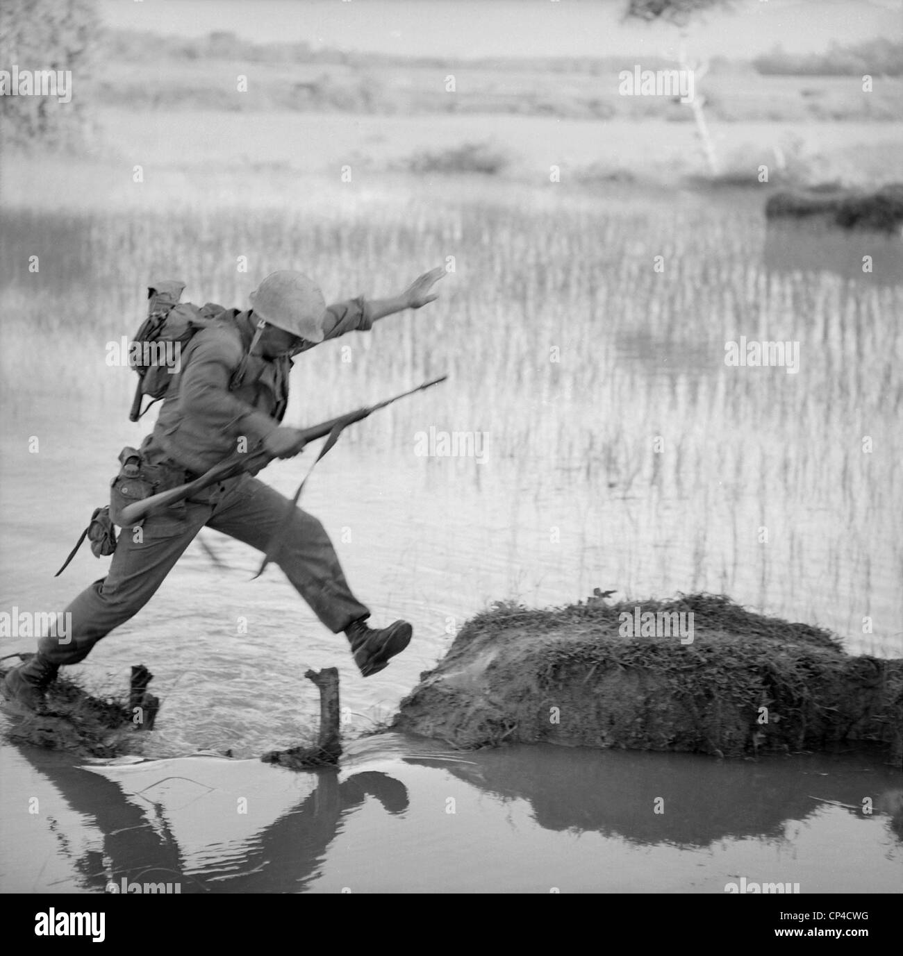 Vietnam War. A US Marine rifleman leaps across a break in a rice paddy dike during a search and destroy mission of Operation Stock Photo