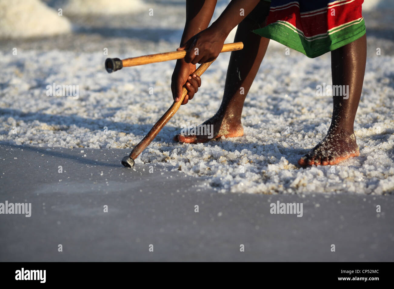 A malagasy  woman in a colourful skirt, breaking the salt crust in the middle of the salt fields near Belo sur Mer Stock Photo