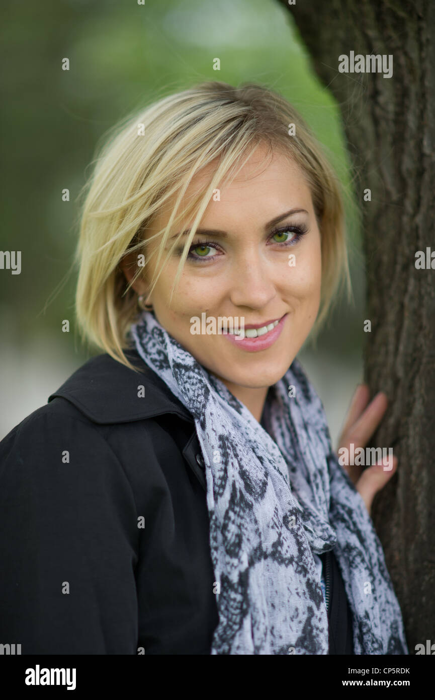 Blond woman leaning against tree Stock Photo