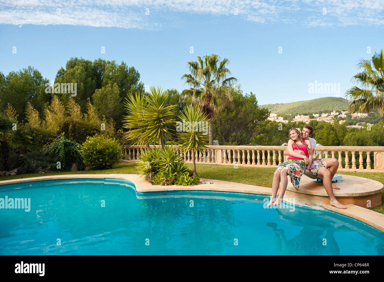 Spain, Mallorca, Couple sitting on diving board at swimming pool, smiling Stock Photo