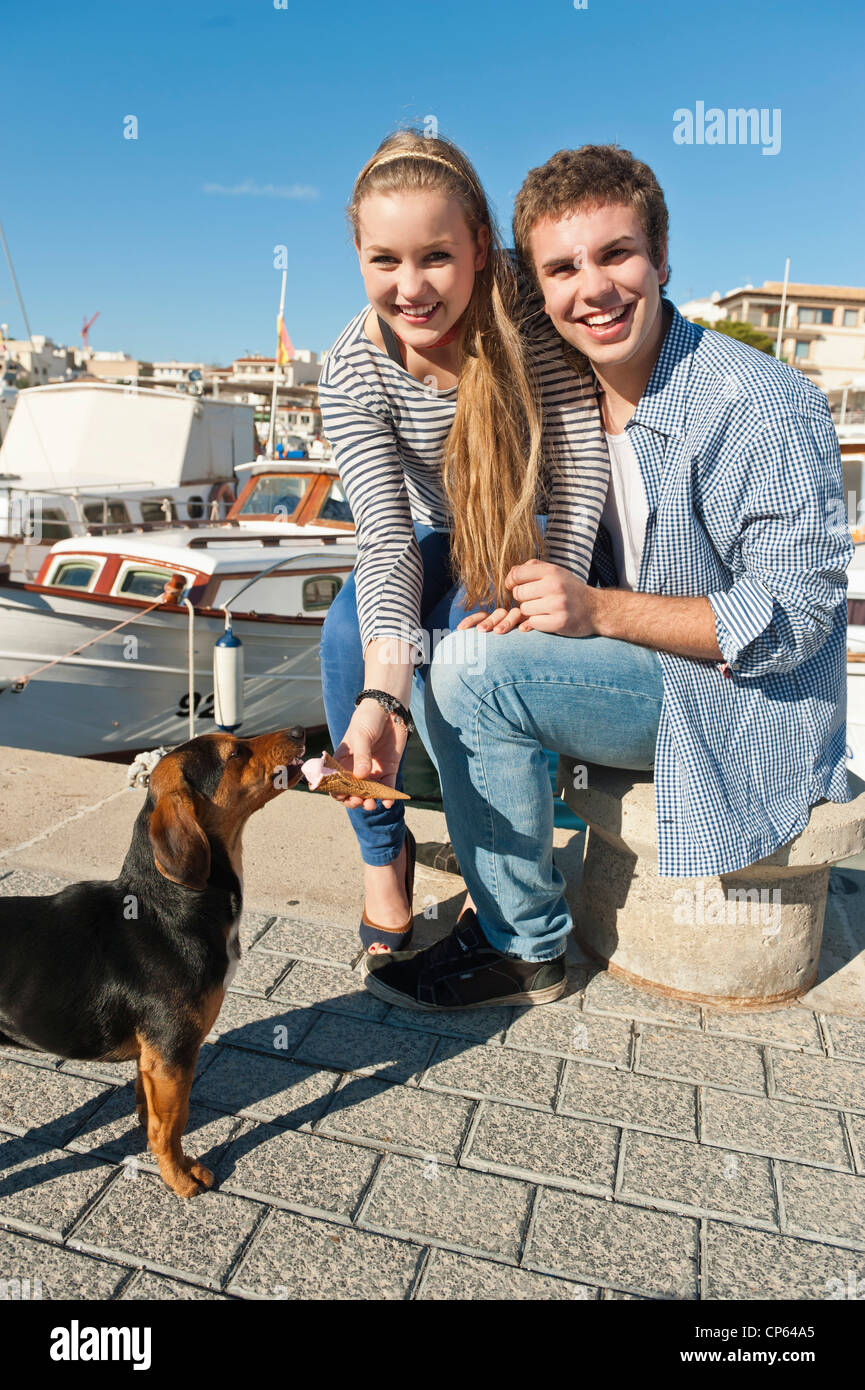Spain, Mallorca, Couple feeding ice cream to stray dog, smiling, portrait Stock Photo