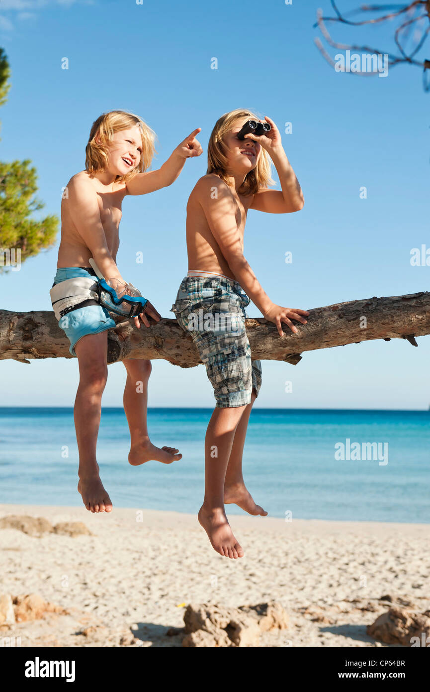 Spain, Mallorca, Children sitting on tree Stock Photo