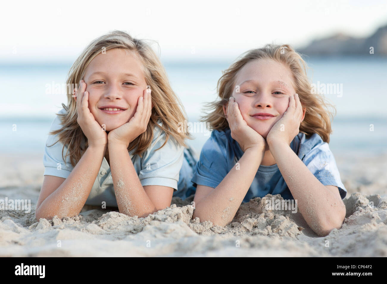 Spain, Mallorca, Children lying in sand on beach, smiling, portrait Stock Photo