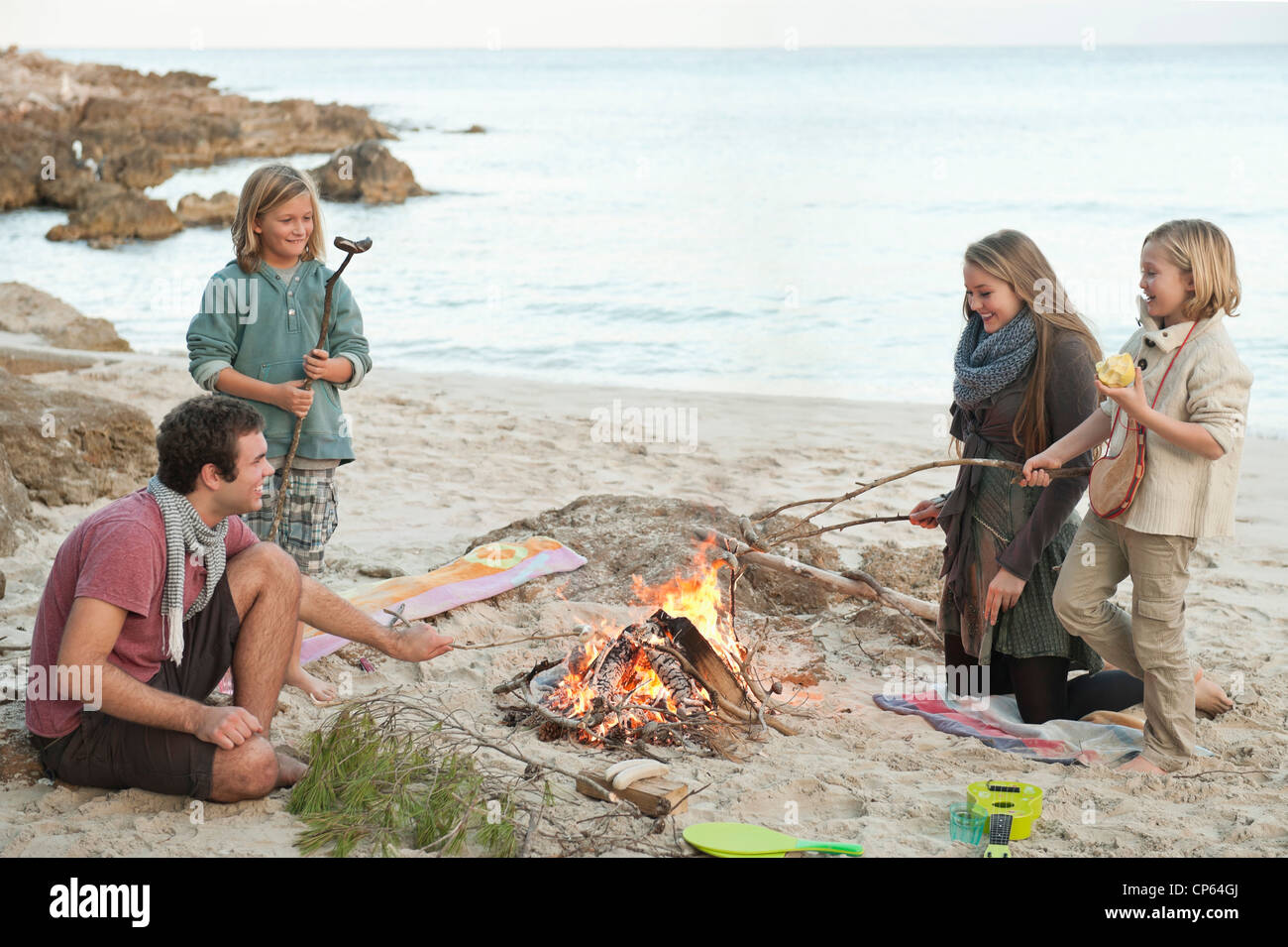 Spain, Mallorca, Friends grilling sausages at camp fire on beach Stock Photo