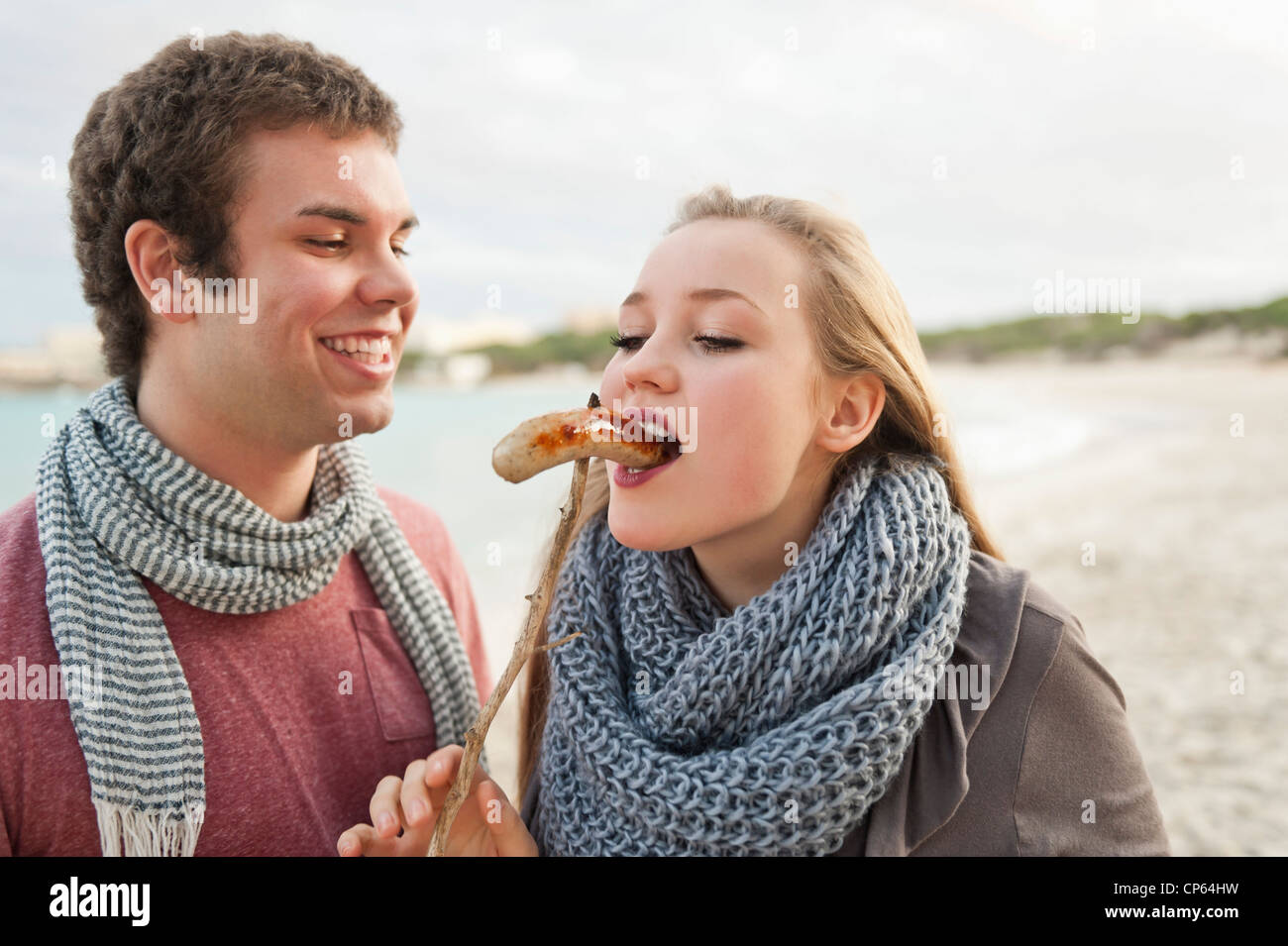 Spain, Mallorca, Young man feeding grilled sausage to teenage girl Stock Photo