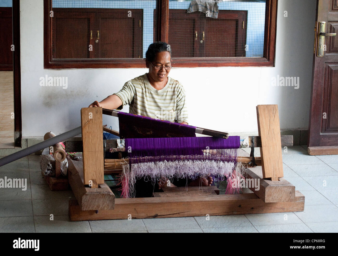 A Balinese woman weaves songket, a type of fabric that has gold an/or silver threads running through the piece on a hand loom. Stock Photo