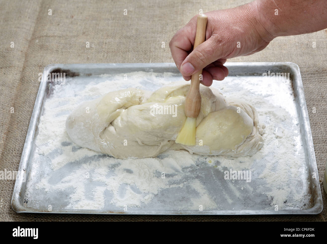 A home baker brushing plaited bread dough with an egg wash Stock Photo