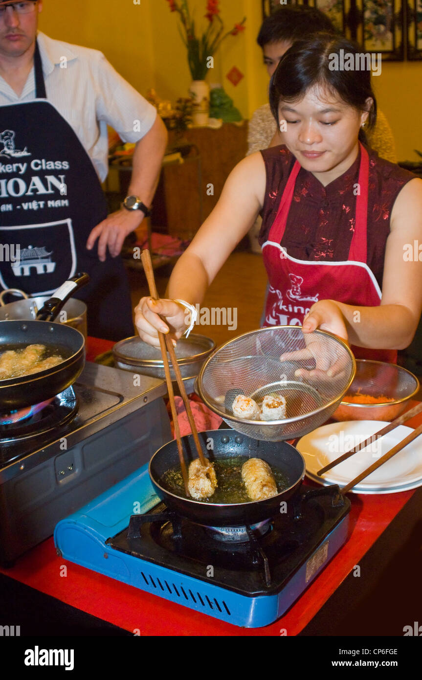 Vertical close up of a Vietnamese chef showing how to fry spring rolls in a cookery lesson. Stock Photo