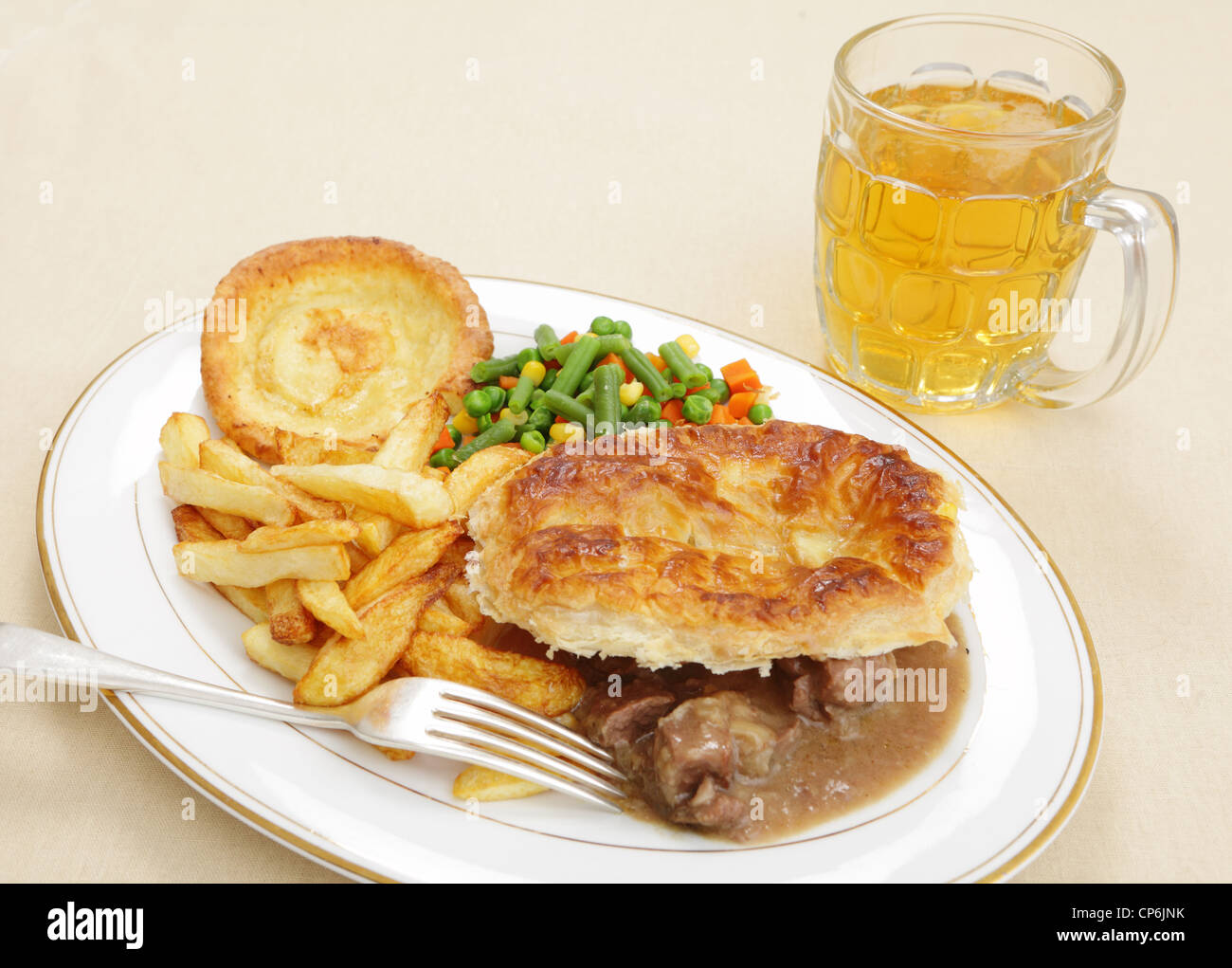 A homemade steak and kidney pie with french fries yorkshire pudding and mixed vegetables served