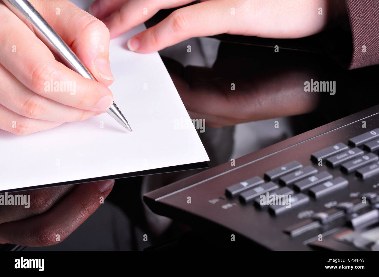 A hand, holding a pen, is ready to write on a document with a telephone next to it. Stock Photo