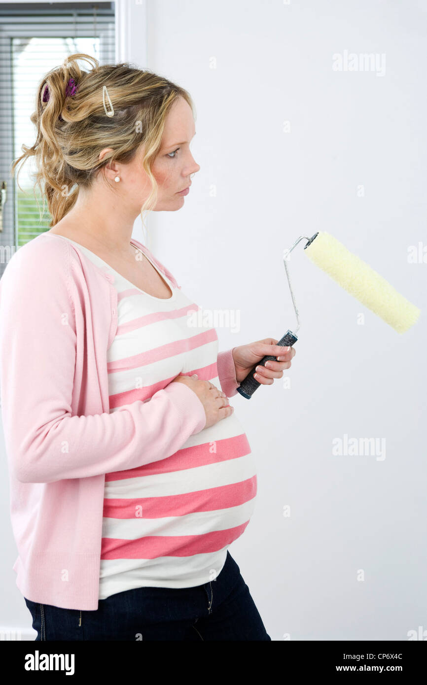 Nine month pregnant woman standing holding a roller paint brush Stock