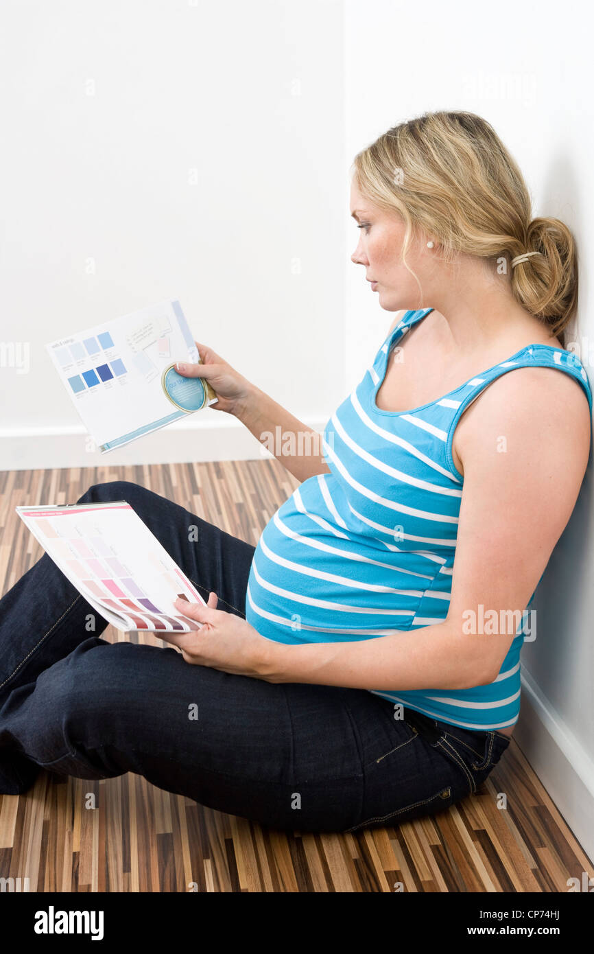 Pregnant woman sitting on the floor of her house looking at paint color