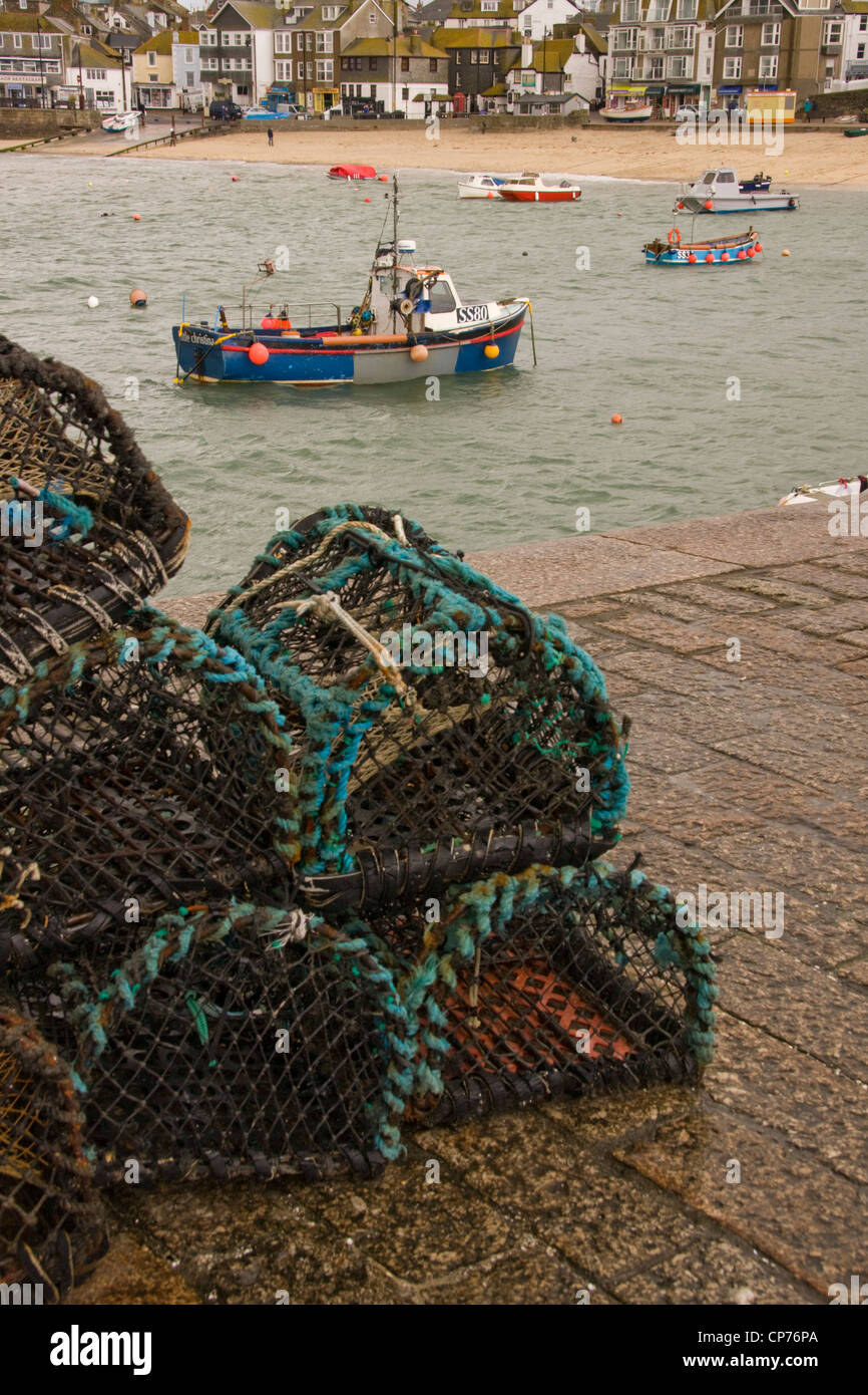 Lobster pots on Smeaton's Pier, St. Ives, Cornwall, with fishing boats in the harbour beyond