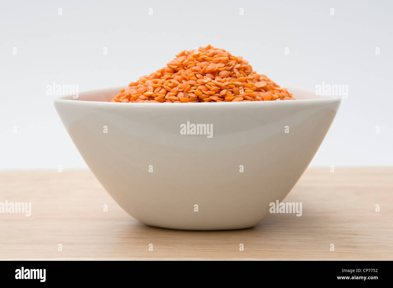Dried red lentils in white bowl on wooden board against a white background Stock Photo