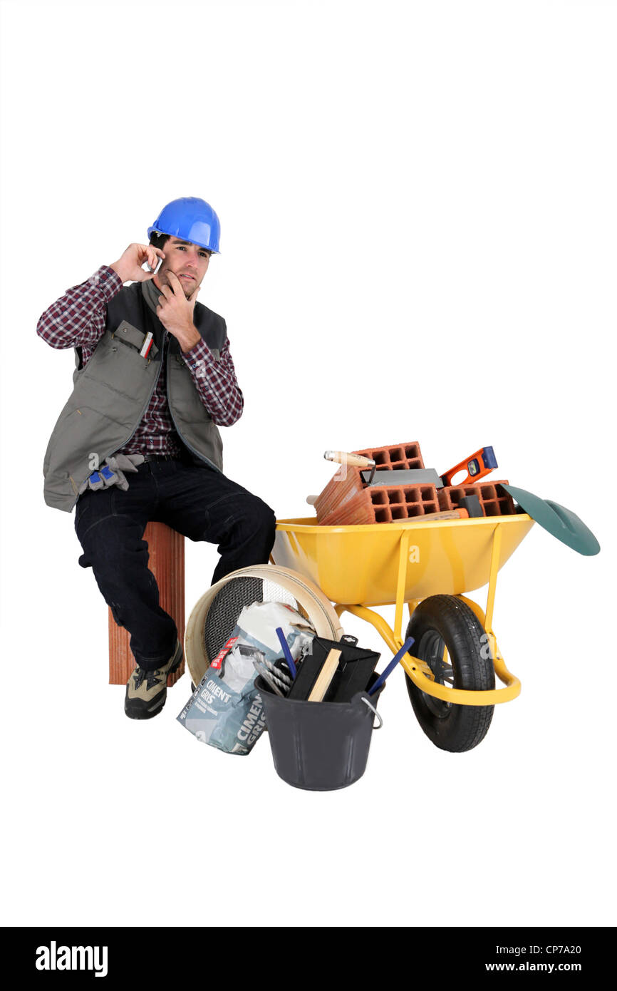 Mans sat making call next to wheelbarrow full of bricks Stock Photo