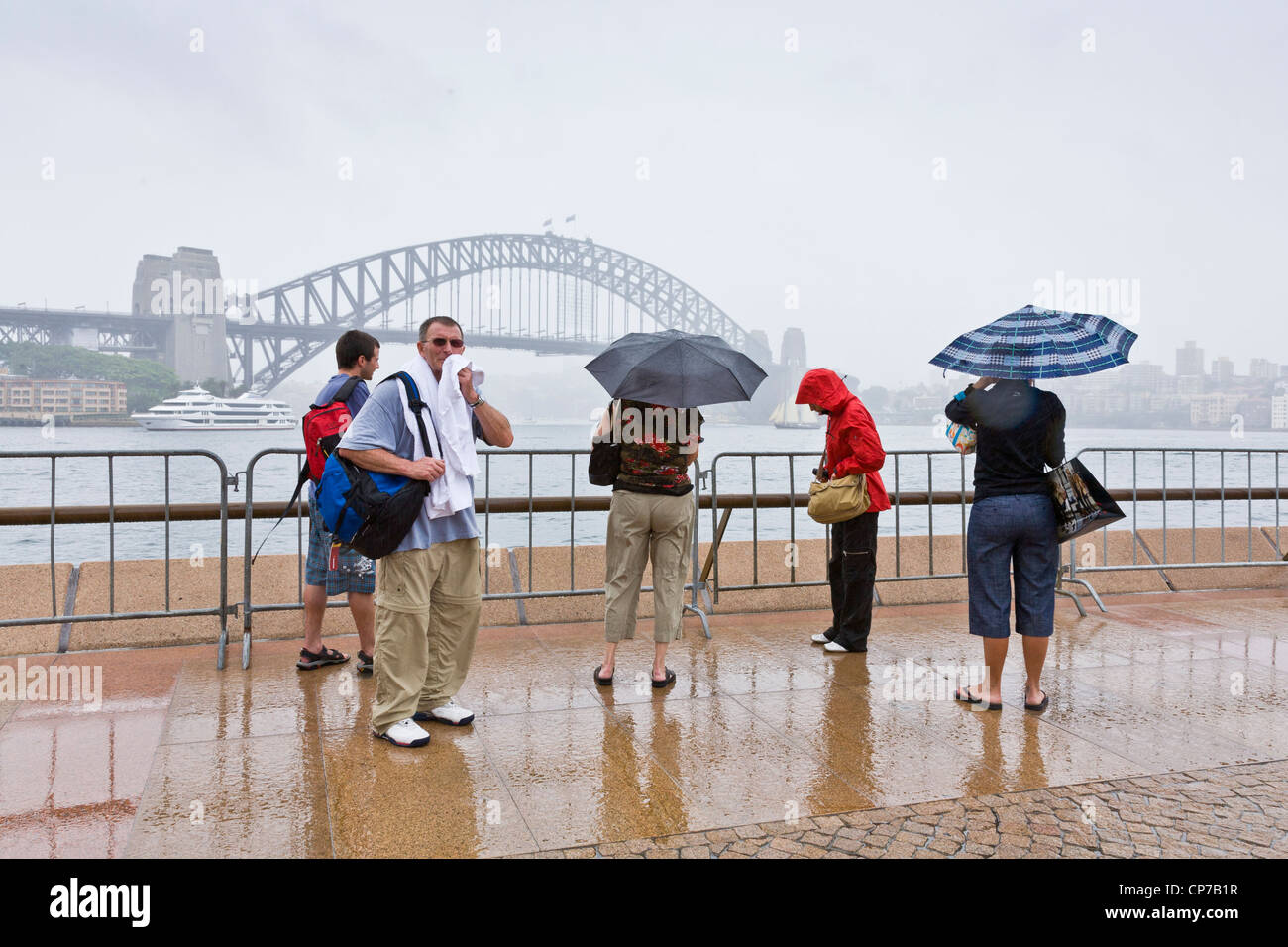A group of tourists looking at Sydney Harbour Bridge on a very wet day. Stock Photo