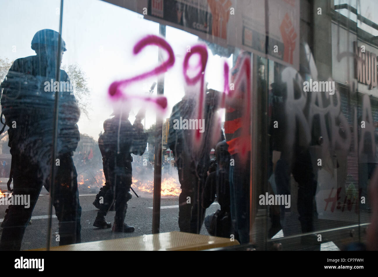 Police, reporters and fire are seen through the spray painted glass of a Barcelona bus stop during the general strike. Stock Photo