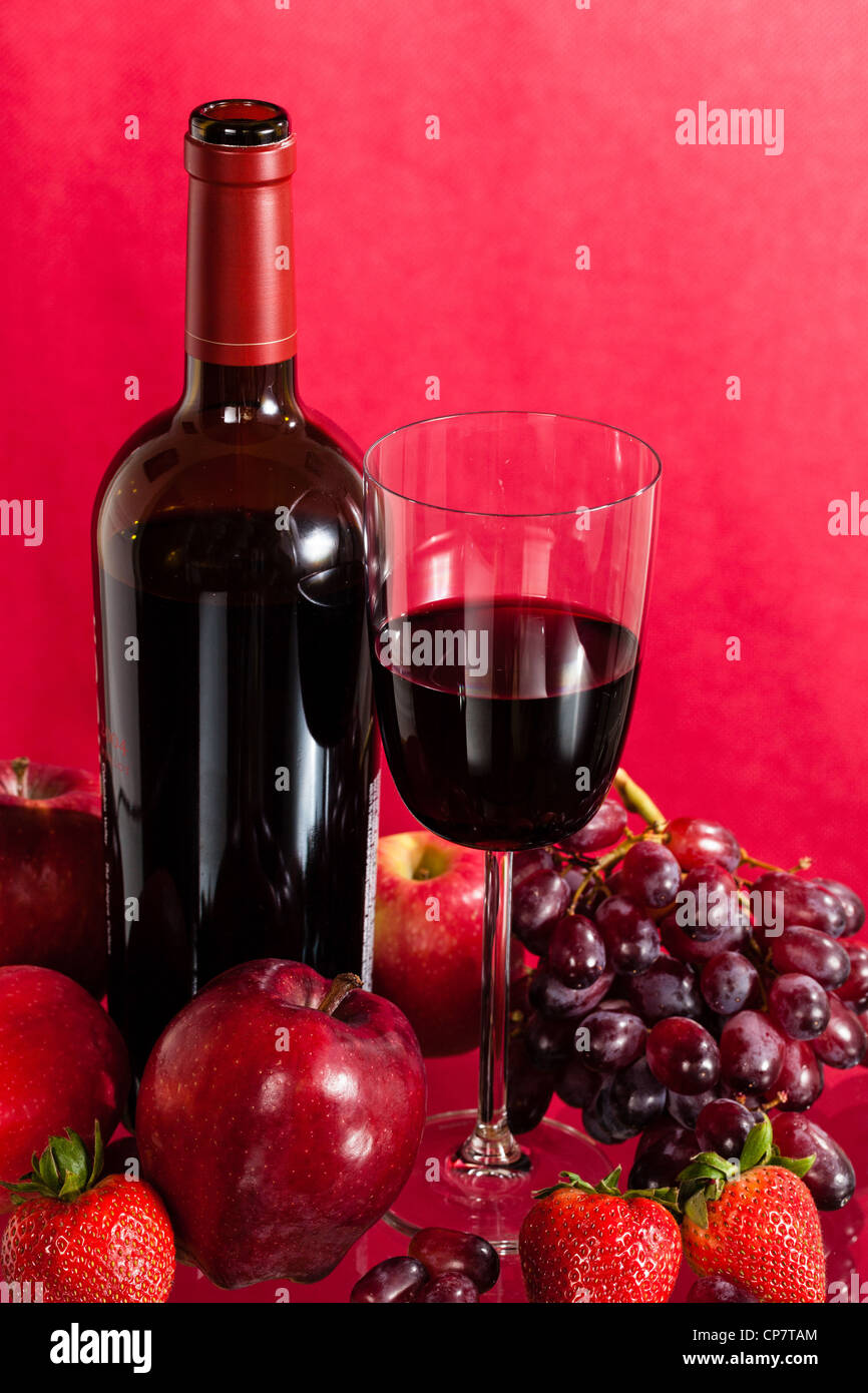 Red wine bottle and red wine in glass with red apples, grapes and
