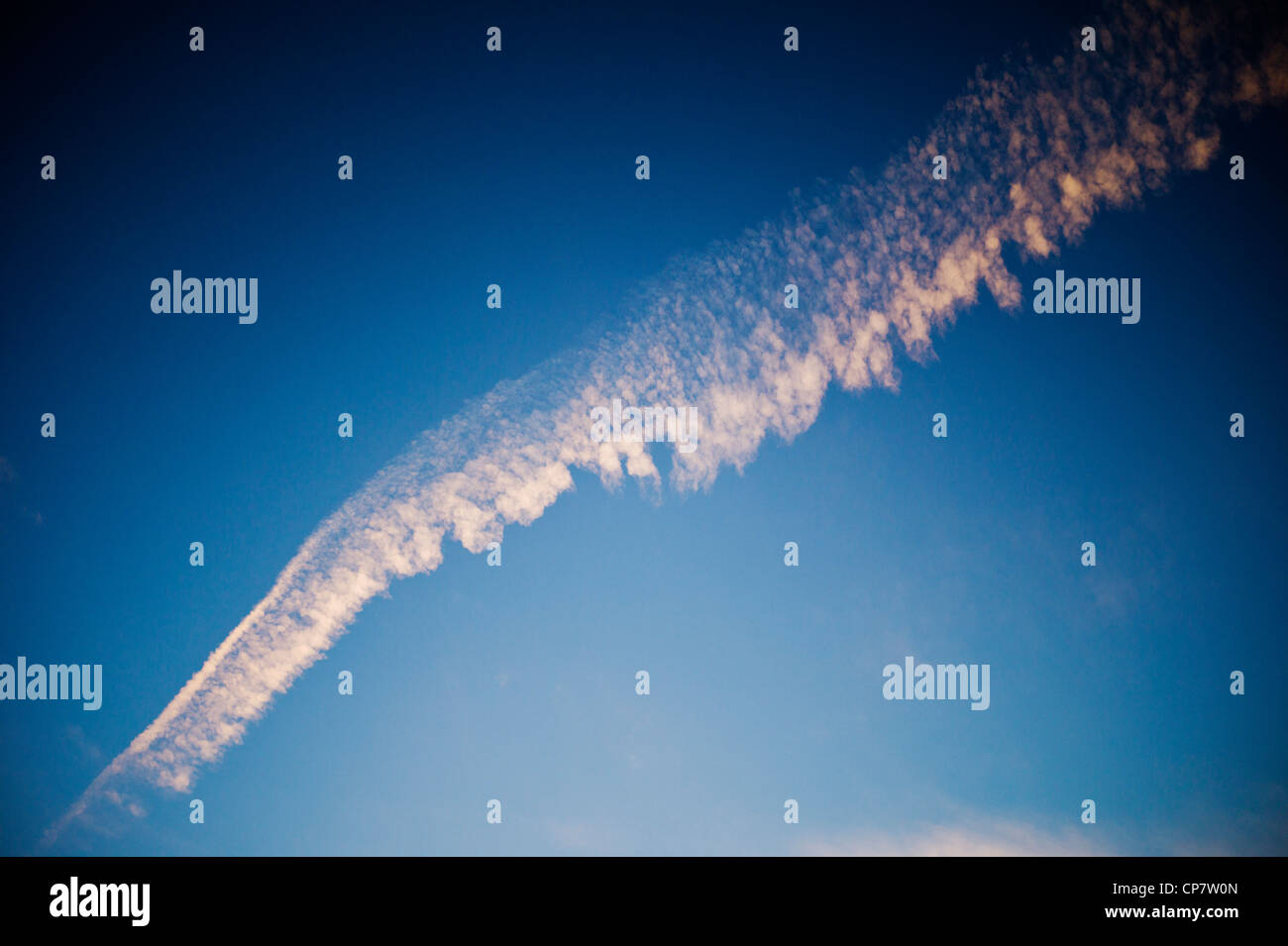 Commercial airline jet contrails across a clear dusk sunset blue sky