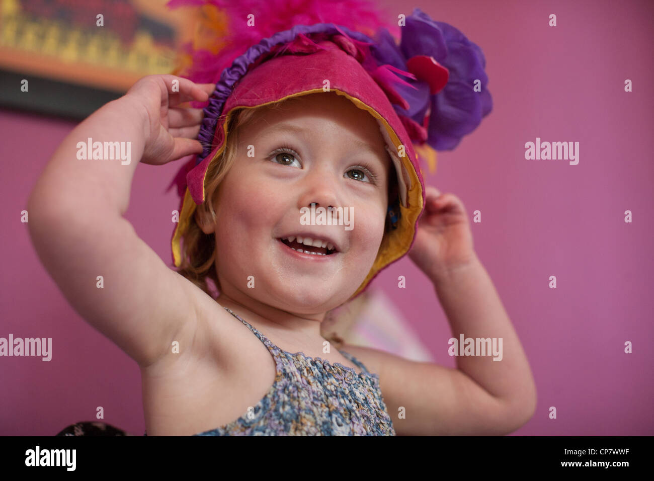 Two year old girl tries on a funny hat while playing dressup in her room. Stock Photo