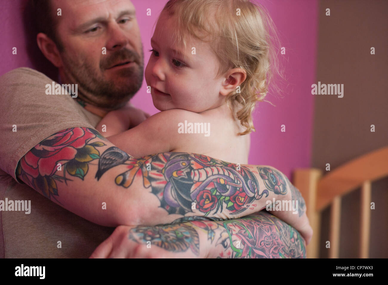 Tattooed dad holds two year old daughter at home in kid's room. Stock Photo