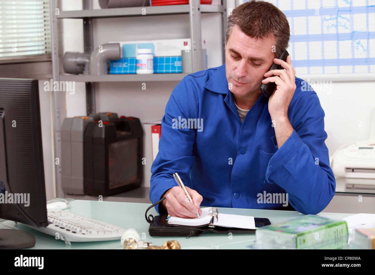 Plumber taking a call in an office and making an appointment in his diary Stock Photo