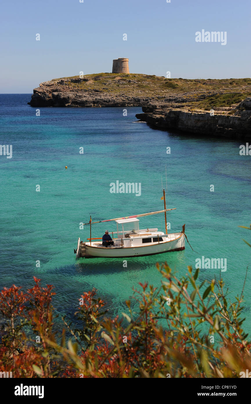 Small fishing boat, or llaut, moored in the inlet of Cala Alcaufar, Menorca, with the Matello Tower in the background Stock Photo