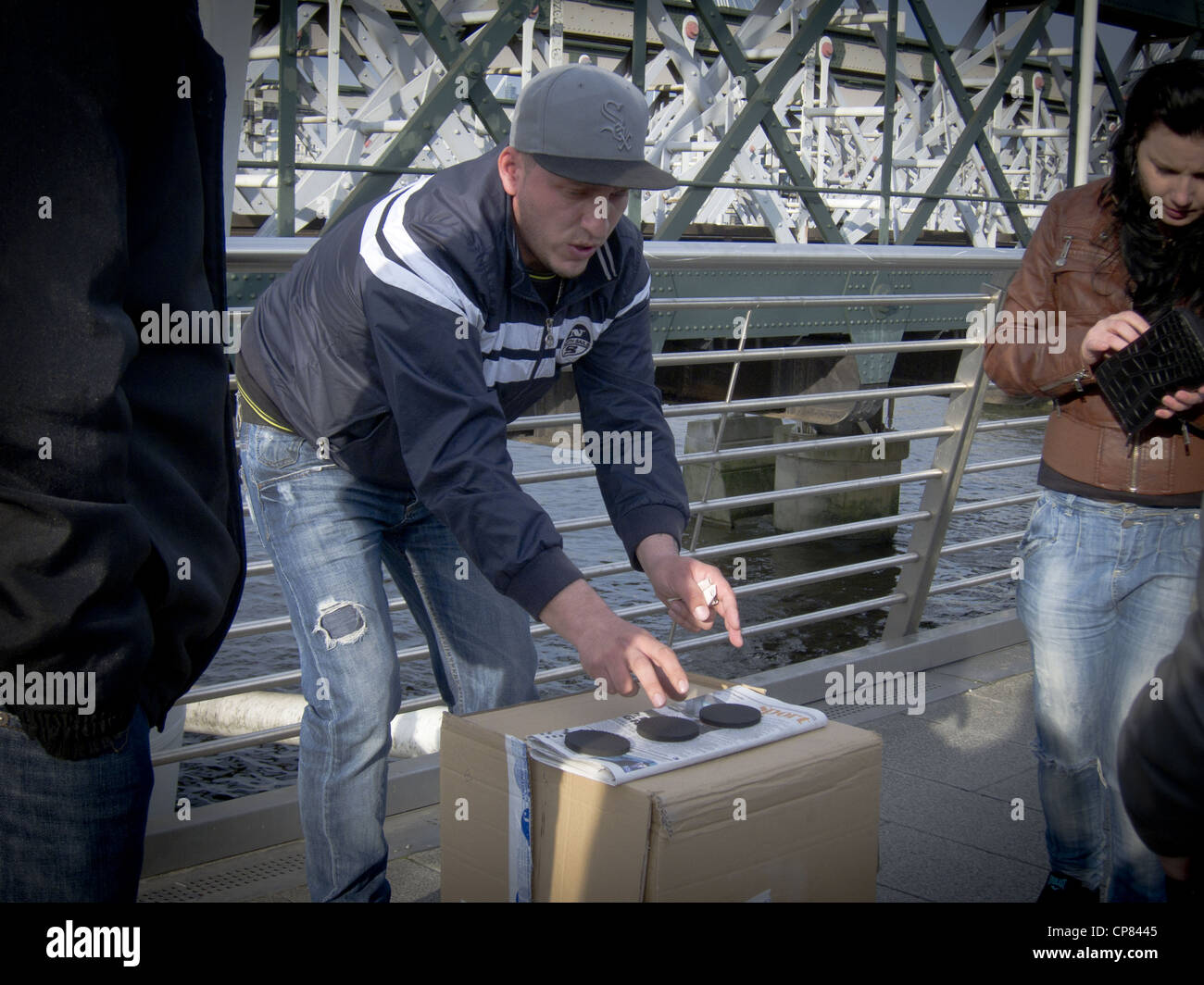 dodgy card sharp trickster playing Three-card Monte Find the lady with a woman about to bet taking moner from her purse Stock Photo