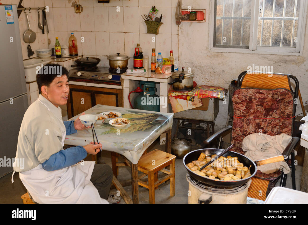 Chinese tofu worker eating lunch in the kitchen in ancient Chengkan village Huangshan Peoples Republic of China Stock Photo