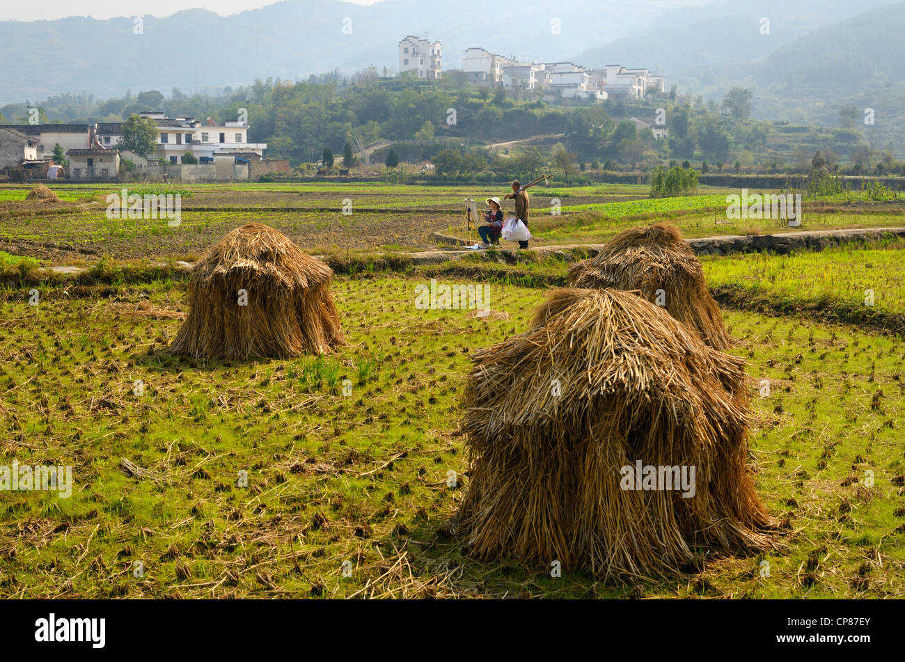 Farmer admiring painting by young Chinese female art student in fields with haystacks Yanggancun hilltop village Huangshan Peoples Republic of China Stock Photo