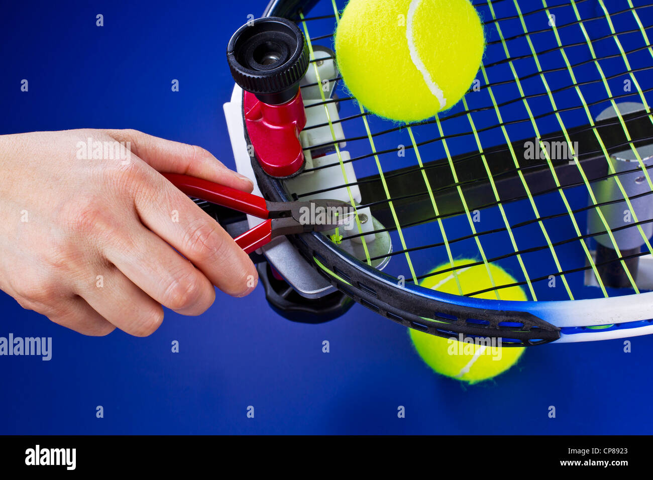 Hand holding pliers while trimming string on tennis racket on blue background Stock Photo