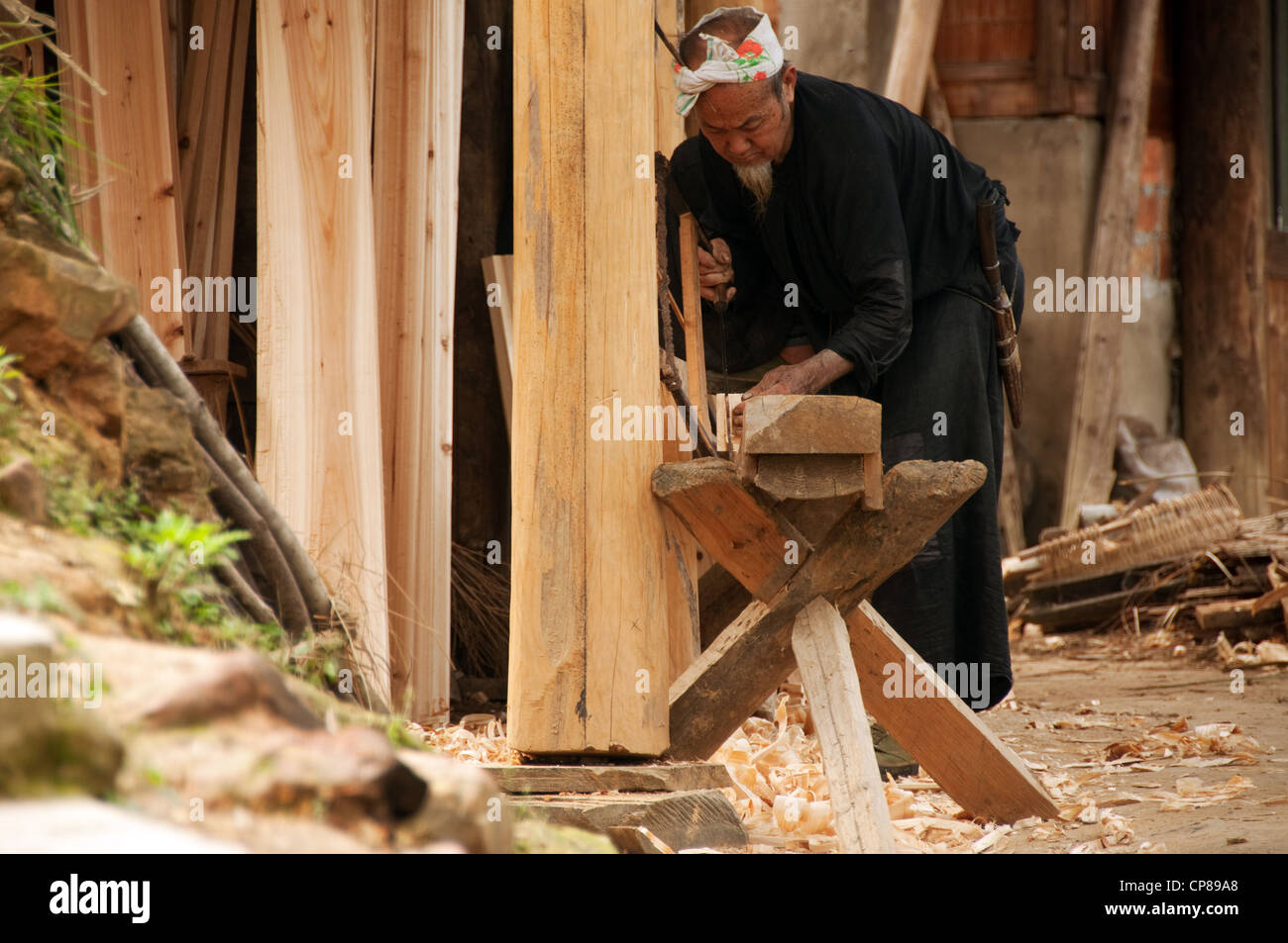 A Basha Miao (Gun Men) man sawing a trunk while building a traditional house, Southern China Stock Photo