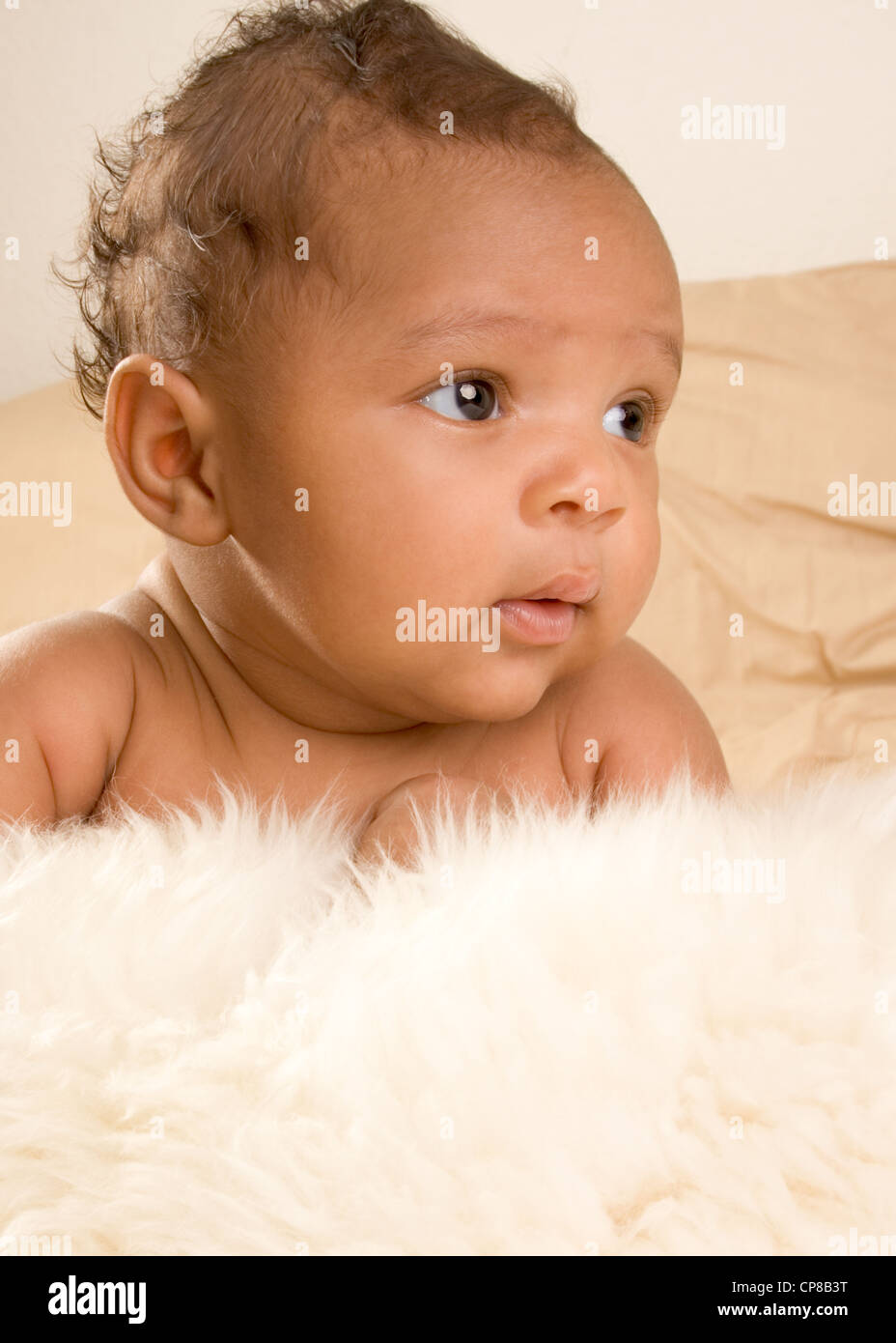 Thoughtful biracial mix of Hispanic and African American infant lying down on fur and yellowish colored blanket Stock Photo