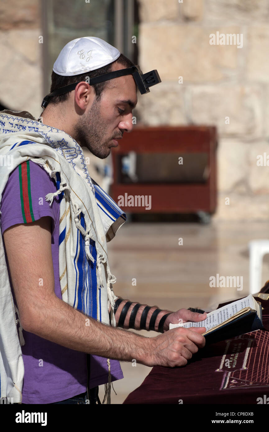 Young Jewish man reading torah wearing kippah, praying shawl & tefillin at Wailing wall, Jerusalem. Israel Stock Photo