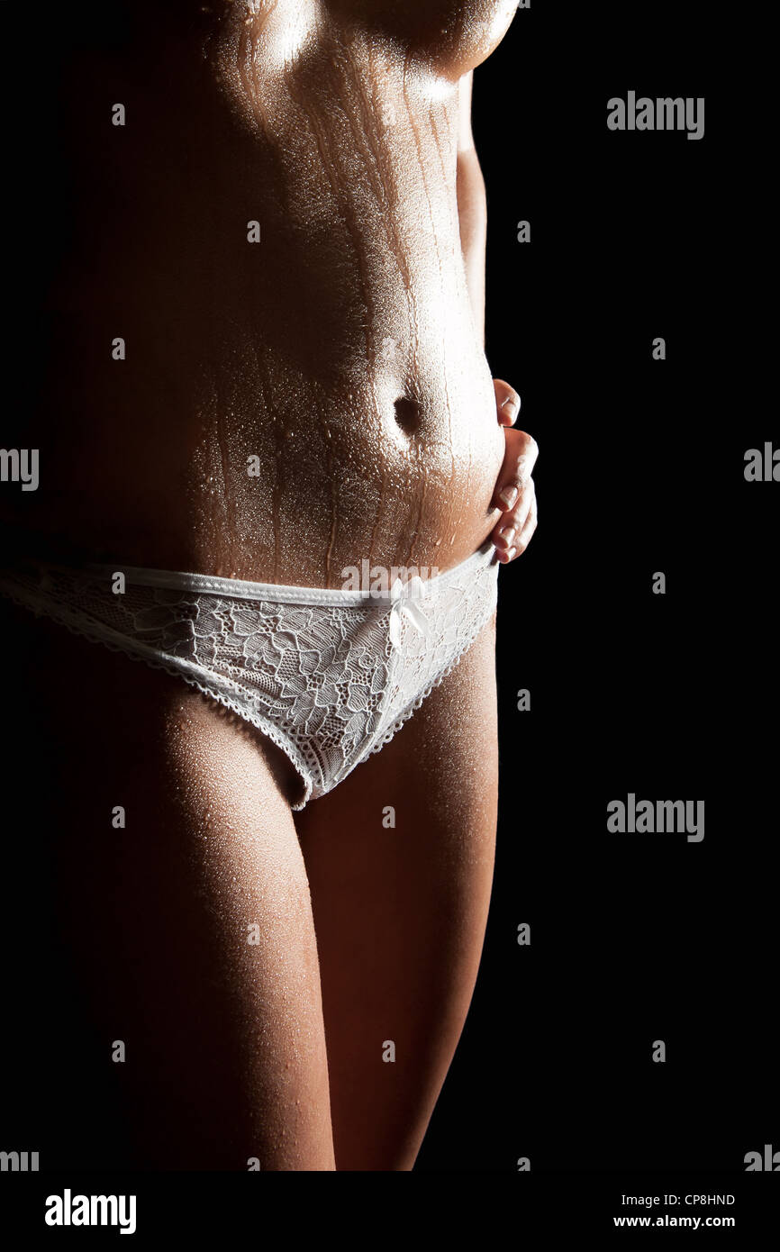 Nude young woman with wet body in beautiful white panties, closeup in front  of black background Stock Photo - Alamy
