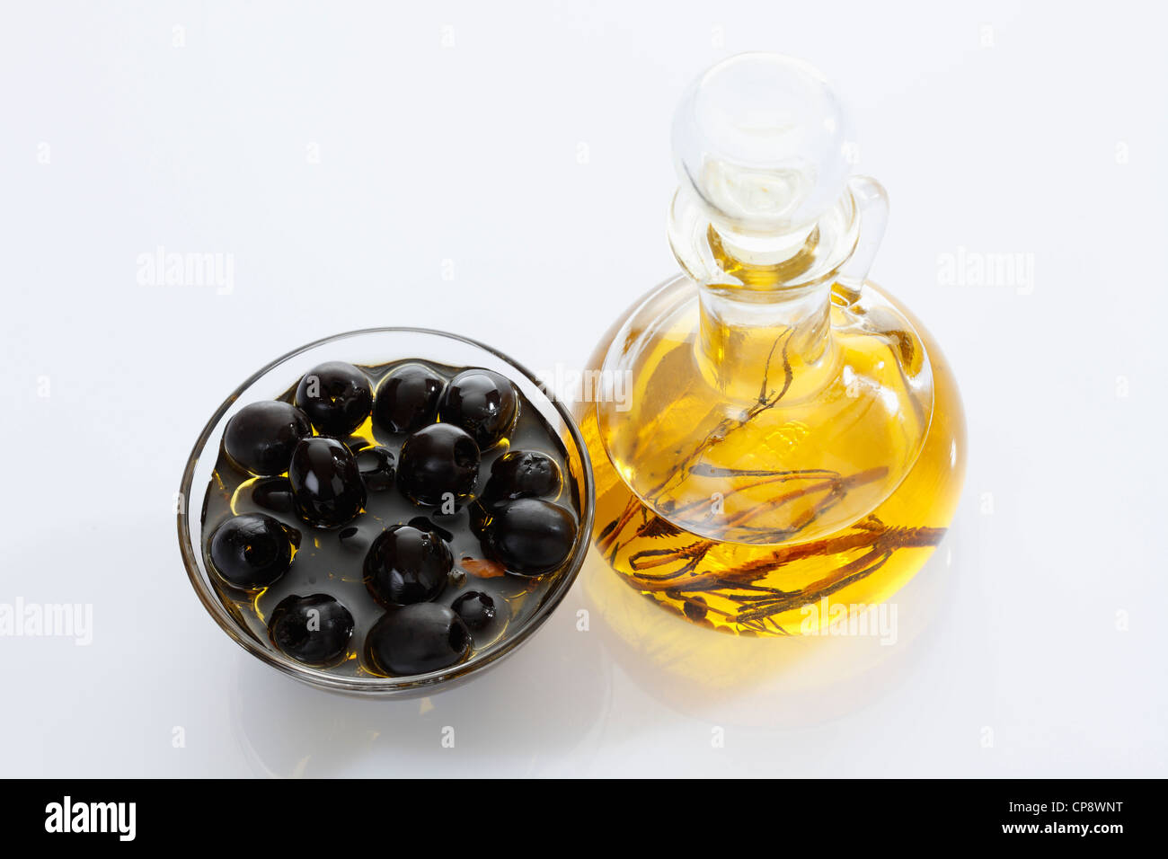 Black olives in glass bowl and bottle of olive oil on white background ...