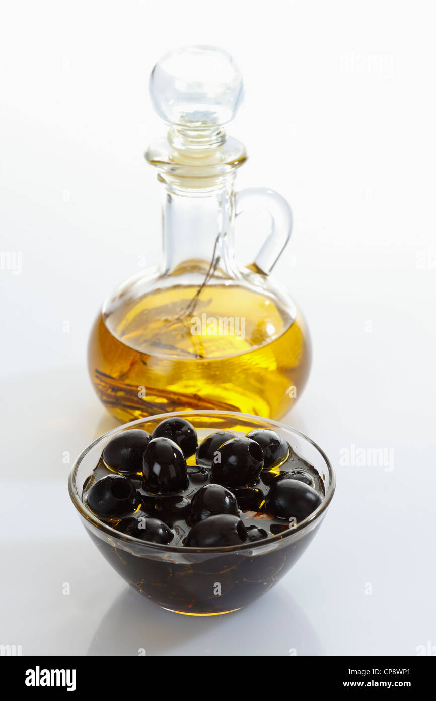 Black olives in glass bowl and bottle of olive oil on white background ...