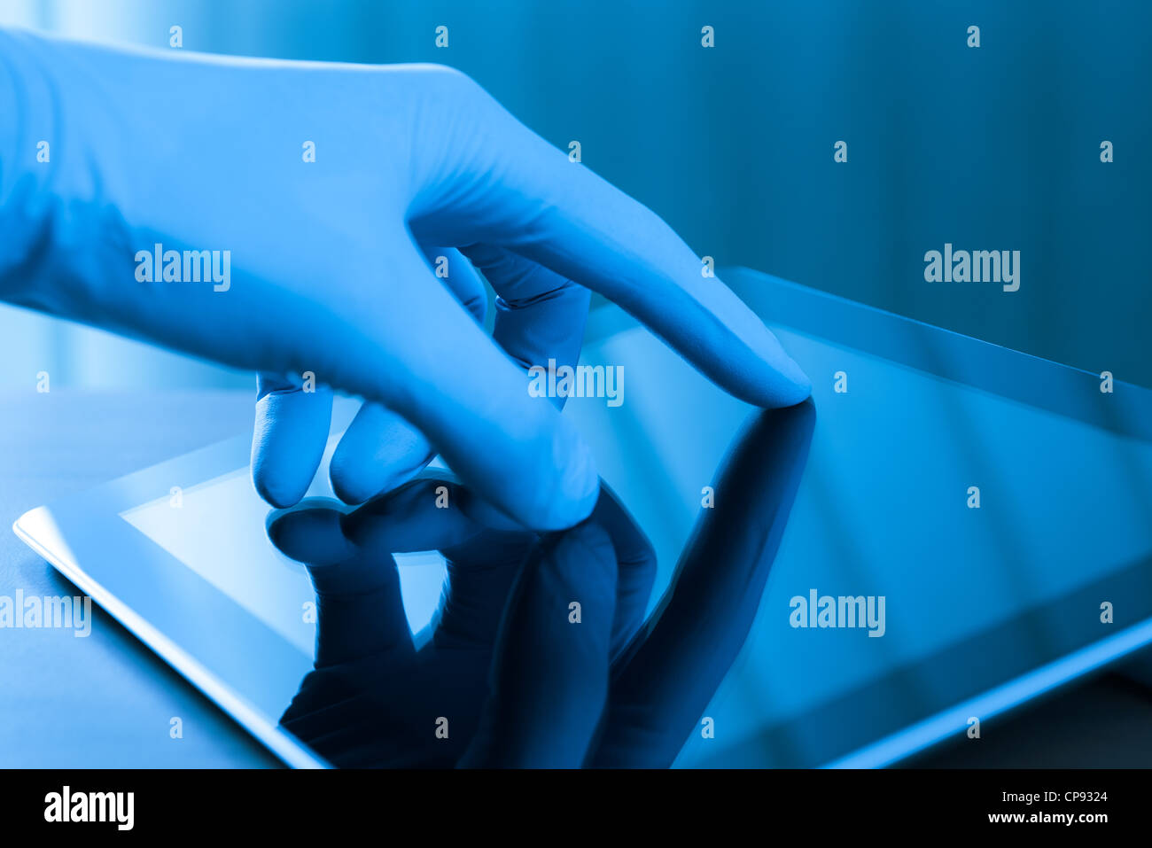Hand in blue glove touching modern digital tablet. Concept image on medical or research theme. Stock Photo
