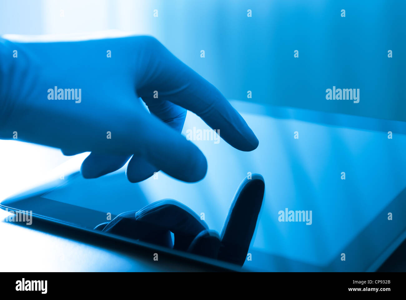 Hand in blue glove touching modern digital tablet. Concept image on medical or research theme. Stock Photo