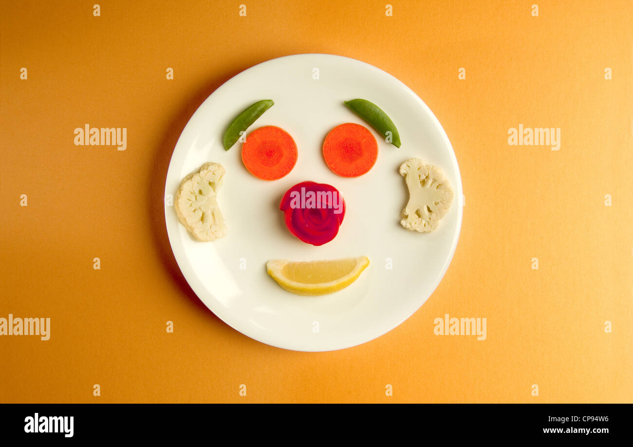 Sliced vegetables arranged as a face on a clean white plate Stock Photo